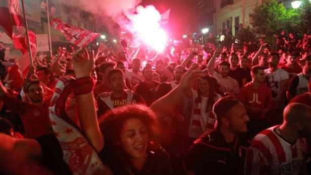 Eine Menschenmenge feiert mit roten Fahnen und Bengalischen Feuern auf einer Straße.
