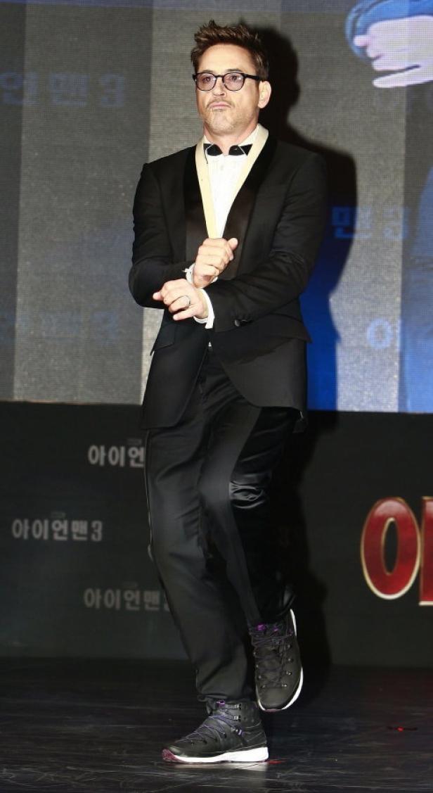 Robert Downey Jr. posiert auf einer Bühne vor einer Werbung für „Iron Man 3“.