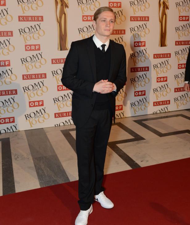 Ein Mann im Anzug und weißen Turnschuhen steht auf einem roten Teppich.