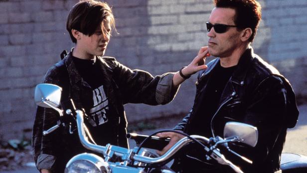 John Connor berührt das Gesicht des Terminators (Arnold Schwarzenegger) auf einem Motorrad.