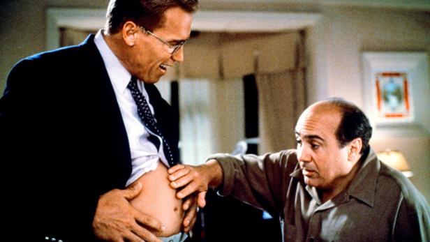 Arnold Schwarzenegger zeigt Danny DeVito seinen Bauch.