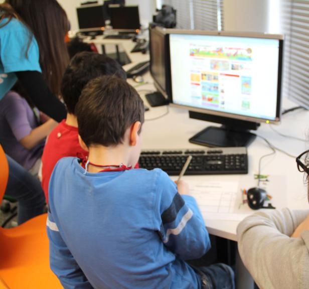 Eine Gruppe von Kindern sitzt an Computern und lernt in einem hellen Raum.