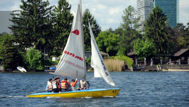 Segeln, Rudern, Tretbootfahren: Die Alte Donau ist ein Paradies für Hobbykapitäne Eine Gruppe von Personen segelt mit einem gelb-blauen Segelboot auf einem See.