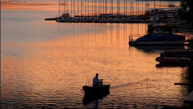 Sonnenuntergang an der Alten Donau Ein Mann fährt bei Sonnenuntergang mit einem kleinen Boot auf einem See.