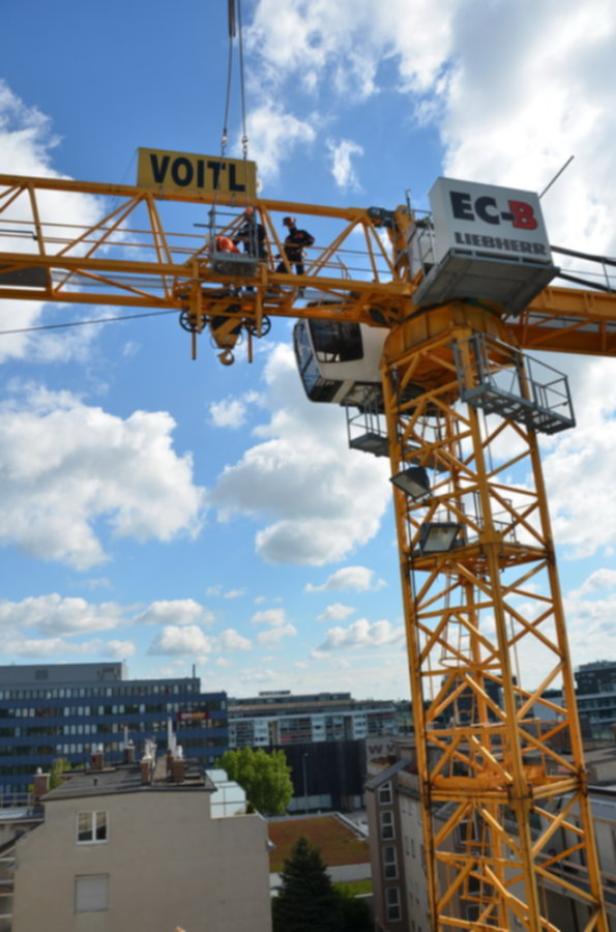 Ein gelber Baukran von Liebherr mit dem Schriftzug „Voitl“ vor blauem Himmel.