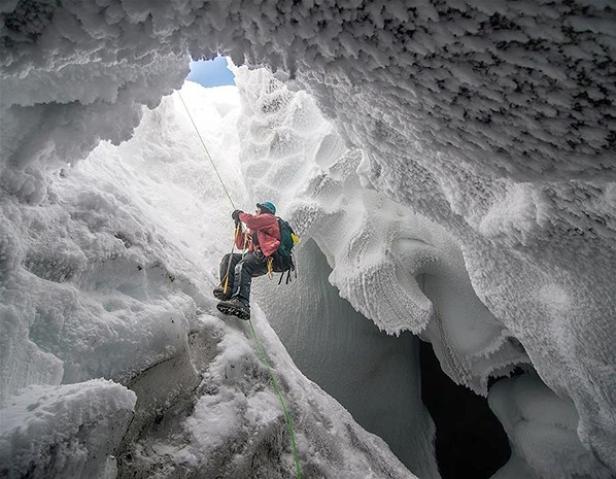 Ein Mann seilt sich in eine schneebedeckte Gletscherspalte ab.