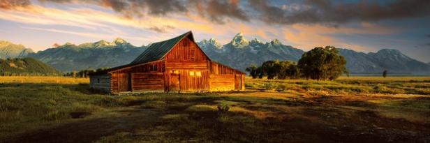 Eine rote Scheune steht vor einer Bergkette in einer weiten Landschaft.