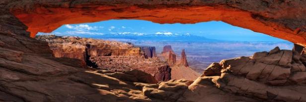 Der Blick durch den Mesa Arch im Canyonlands Nationalpark auf schneebedeckte Berge.