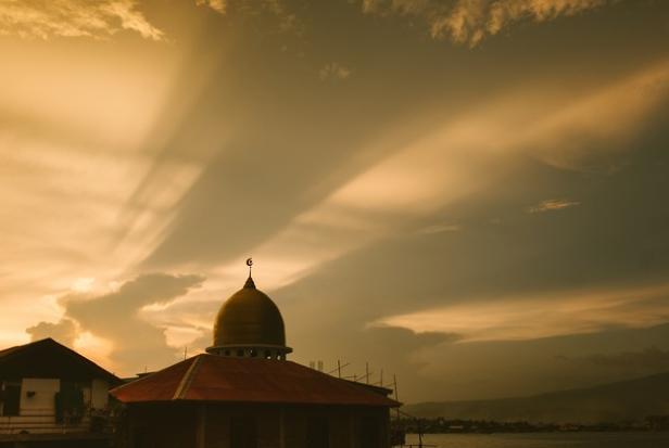 Eine Moschee mit goldener Kuppel unter einem dramatischen Himmel bei Sonnenuntergang.