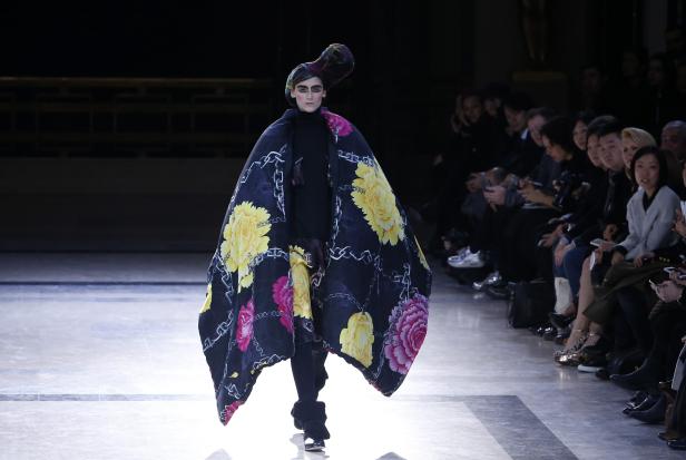 Ein Model präsentiert ein extravagantes Cape mit Blumenmuster auf dem Laufsteg.