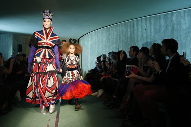 Zwei Models präsentieren extravagante Mode auf einem Laufsteg vor Publikum.