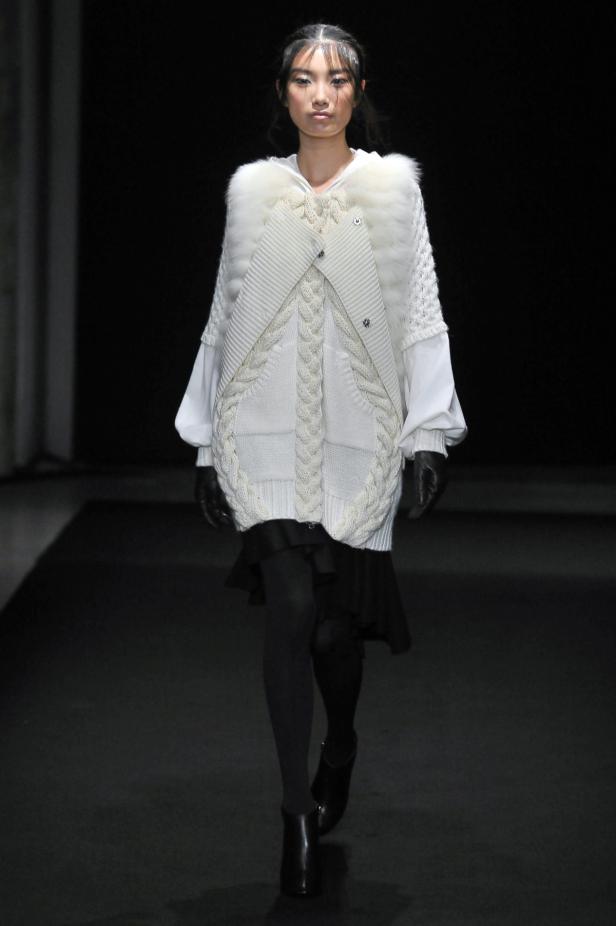 Eine Frau präsentiert ein weißes Strickkleid mit Pelzkragen auf dem Laufsteg.