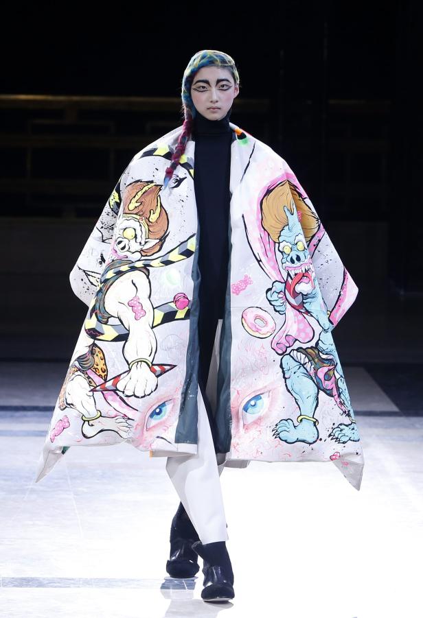 Ein Model mit farbigem Haar trägt einen Mantel mit Cartoon-Motiven auf dem Laufsteg.