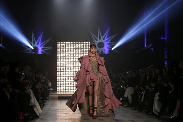 Eine Frau mit Gesichtsbemalung präsentiert ein extravagantes Outfit auf dem Laufsteg.