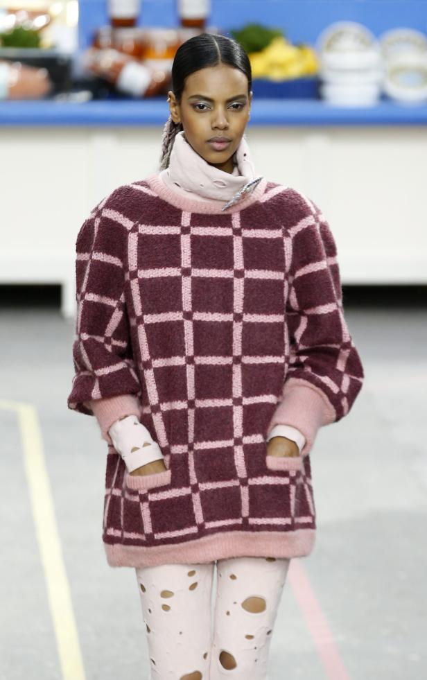 Eine Frau präsentiert einen karierten Pullover und rosafarbene Leggings mit Löchern auf einem Laufsteg.