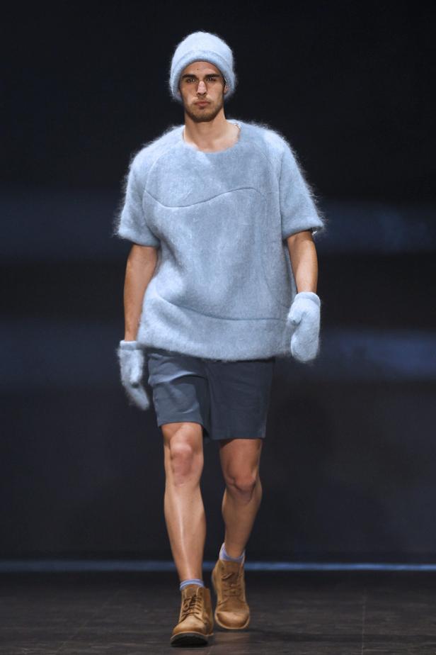 Ein Mann in einem hellblauen, flauschigen Outfit mit Mütze und Handschuhen läuft auf einem Laufsteg.