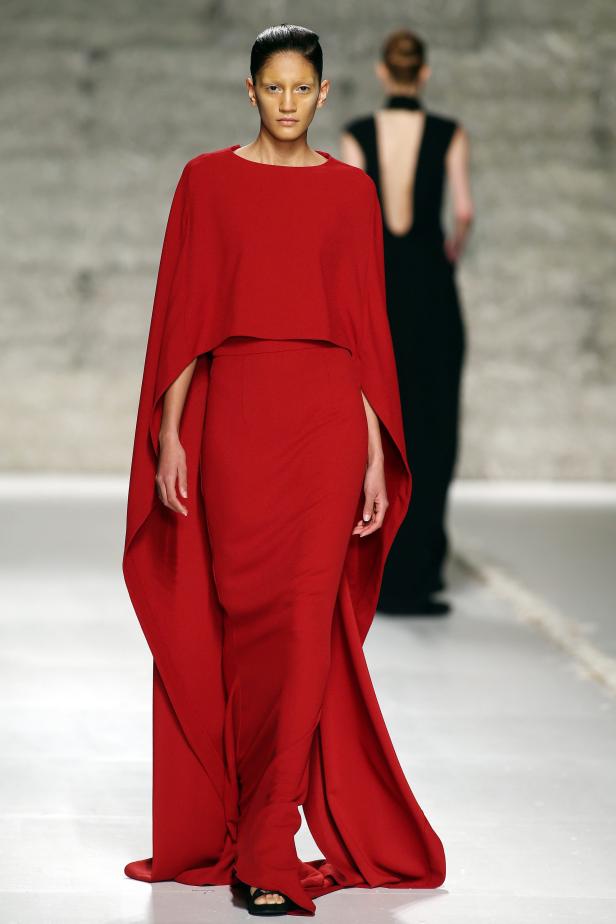 Eine Frau in einem roten Kleid mit Cape auf einem Laufsteg.