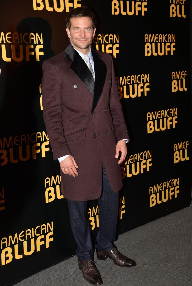 Bradley Cooper posiert vor einer Wand mit dem Schriftzug „American Bluff“.