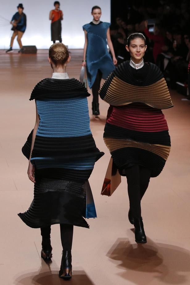 Models präsentieren farbenfrohe, plissierte Kleider auf einem Laufsteg.