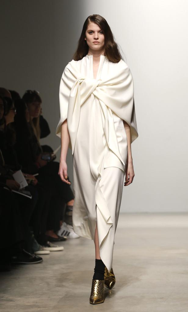 Eine Frau präsentiert ein weißes Kleid mit einem großen Knoten auf dem Laufsteg.