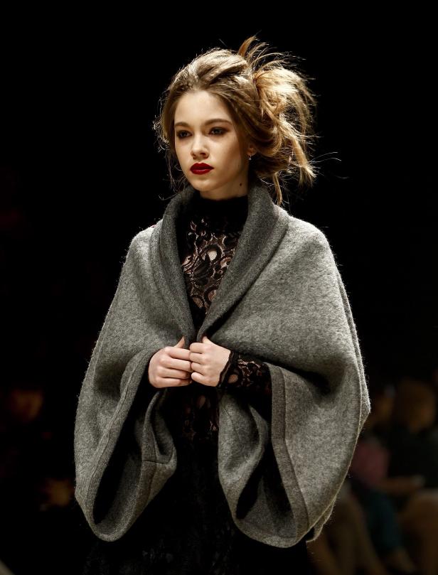 Eine junge Frau mit rotem Lippenstift und einem grauen Umhang.