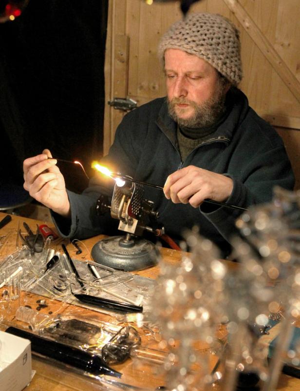 Ein Glasbläser formt mit einer Flamme eine Glasstange.