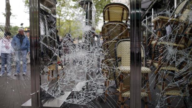 Die zerbrochene Scheibe eines Cafés in Paris mit gestapelten Stühlen im Hintergrund.