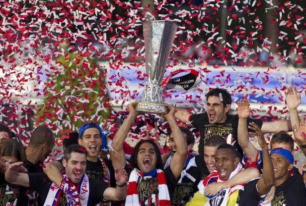 Fußballspieler feiern einen Sieg mit Konfetti und dem Pokal in der Hand.