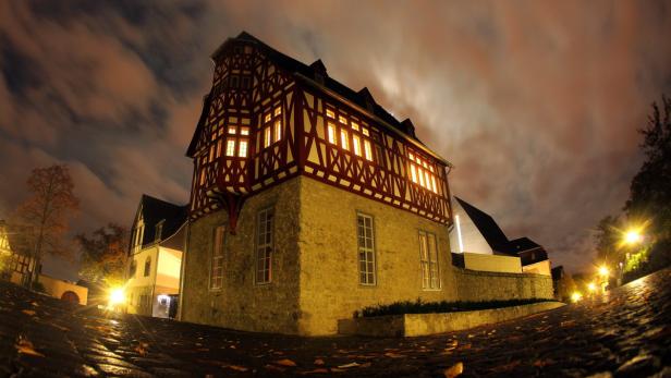 Ein Fachwerkhaus mit beleuchteten Fenstern in einer Stadt bei Nacht.