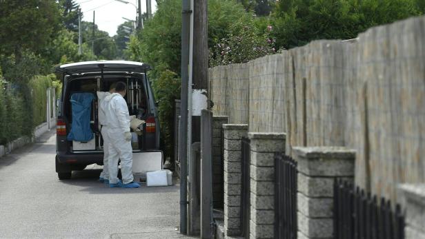 Zwei Personen in Schutzanzügen stehen an einem Lieferwagen auf einer Wohnstraße.