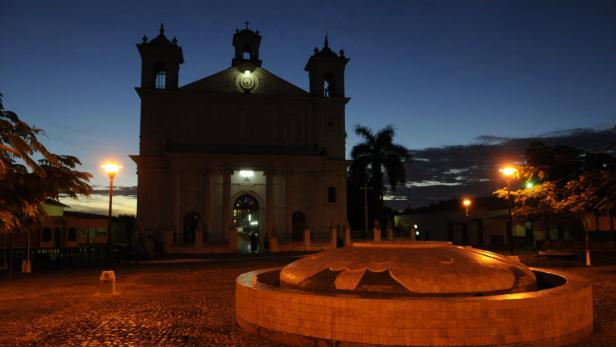 Eine Kirche und ein Brunnen sind nachts beleuchtet.