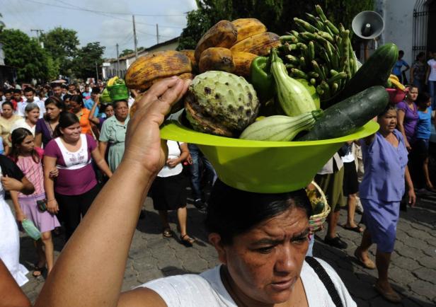 Eine Frau balanciert eine Schüssel mit Obst und Gemüse auf dem Kopf.