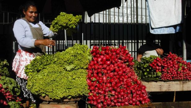 Eine Frau verkauft Salat und Radieschen auf einem Marktstand.