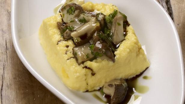 Polenta mit Pilzen und Kräutern auf einem weißen Teller.