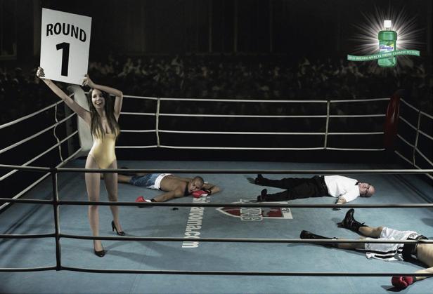 Ein Boxring mit K.O.-geschlagenen Kämpfern und einem Ring Girl, das die erste Runde ankündigt.