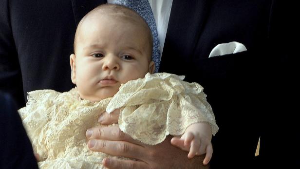 Prinz George in einem cremefarbenen Taufkleid auf dem Arm eines Mannes.
