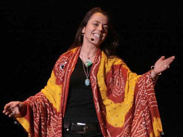 Eine Frau mit Mikrofon und einem gelb-roten Tuch gestikuliert auf einer Bühne.