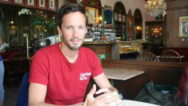 Klaus Schwertner Ein Mann mit rotem T-Shirt sitzt in einem traditionellen Café.