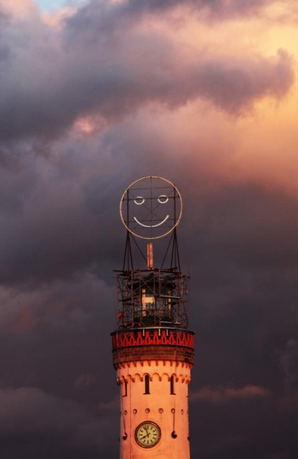 Ein Turm mit einer lächelnden Smiley-Gesichts-Installation unter einem dramatischen Himmel.