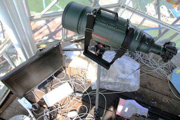 Ein großes Sigma-Teleobjektiv ist auf einem Stativ in einem Raum mit einem Monitor aufgebaut.