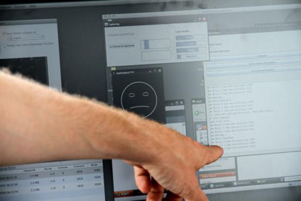 Ein Arm zeigt auf einen Computerbildschirm mit verschiedenen Fenstern, darunter ein trauriger Smiley.