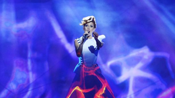 Eine Sängerin mit kurzem, blondem Haar singt auf einer Bühne mit blauem Hintergrund.