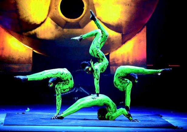 Eine Gruppe von Akrobaten in grünen Kostümen führt eine Performance auf einer Bühne auf.