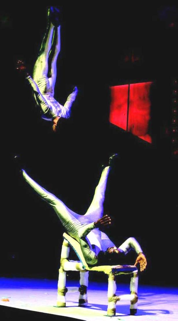 Zwei Akrobaten in silbernen Anzügen führen eine beeindruckende Darbietung auf einer Bühne auf.