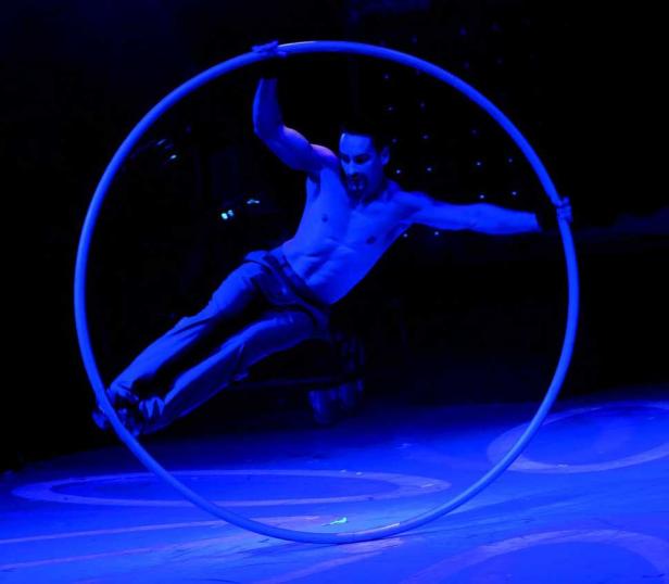 Ein Mann turnt in einem blau beleuchteten Zirkusreifen.