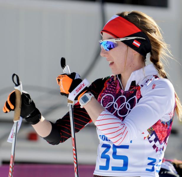 Eine Langläuferin mit Stirnband und Skibrille hält ihre Skistöcke.