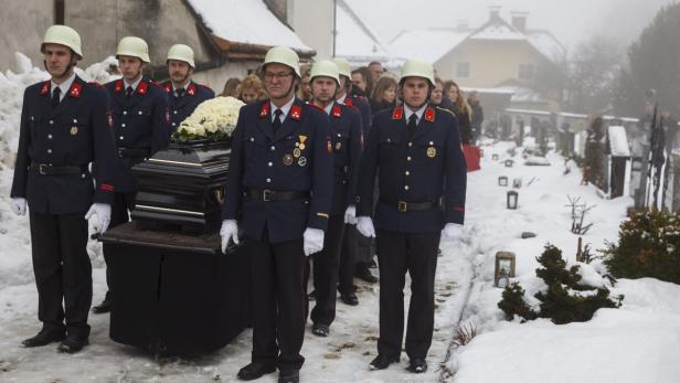 Feuerwehrleute tragen einen Sarg durch einen verschneiten Friedhof.