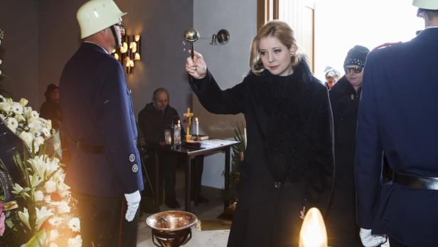 Eine Frau sprengt Weihwasser in einem Raum, in dem eine Trauerfeier stattfindet.