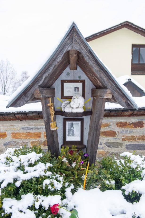 Ein hölzerner Bildstock mit Fotos, einer Engelsfigur und winterlicher Dekoration im Schnee.