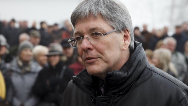 Ein Mann mit Brille steht vor einer Menschenmenge.